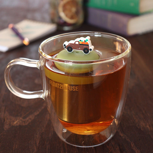 brown pumpkin truck tea infuser for loose leaf tea with a fine mesh stainless steel tea infuser that reads FLOAT2INFUSE on a green base floating in a glass tea mug with pen on notebook and loose leaf tea and books in the background