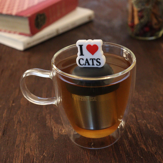 black text on white background that reads "i love cats" with red heart tea infuser for loose leaf tea on a black base with a fine mesh stainless steel tea infuser that reads FLOAT2INFUSE floating in a glass tea mug with books and loose leaf tea in the background