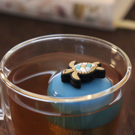 sea turtle animal tea infuser for loose leaf tea on a blue base floating in a glass tea mug with books in the background