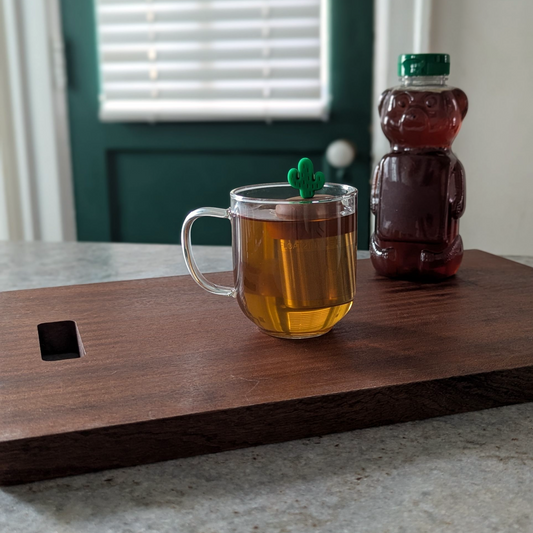 green cactus tea infuser for loose leaf tea with fine mesh stainless steel tea strainer that reads FLOAT2INFUSE on a brown base floating in a glass tea mug with a honey bear in the background