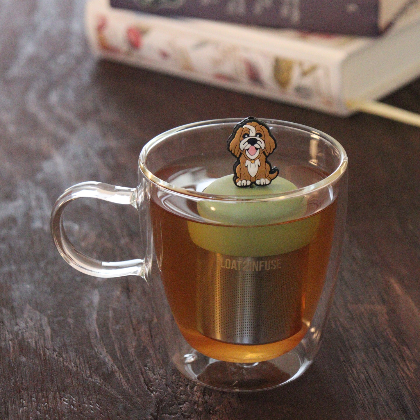 brown golden retriever dog animal tea infuser for loose leaf tea with a fine mesh stainless steel tea infuser that reads FLOAT2INFUSE on a green base floating in a glass tea mug with books in the background
