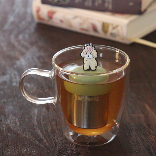 pink bow poodle dog animal tea infuser for loose leaf tea on a green base with a fine mesh stainless steel tea infuser that reads FLOAT2INFUSE floating in a glass tea mug with books in the background