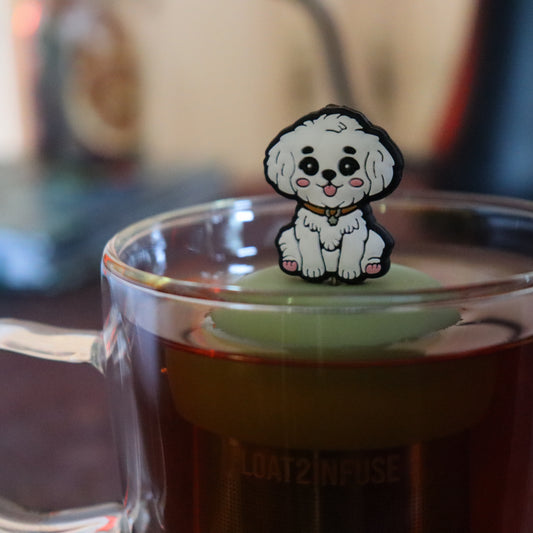 white maltipoo dog animal tea infuser for loose leaf tea on a green base with a fine mesh stainless steel tea strainer that reads FLOAT2INFUSE floating in a glass tea mug with tea kettle in the background