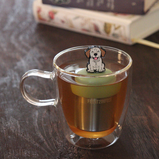 yellow Labrador Retriever dog animal tea infuser for loose leaf tea with a fine mesh stainless steel tea infuser that reads FLOAT2INFUSE on a green base floating in a glass tea mug with books in the background