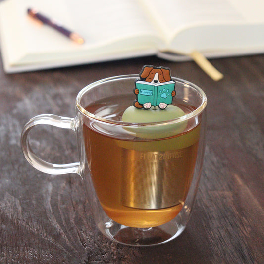 brown dog reading green book animal tea infuser for loose leaf tea on a green base with a fine mesh stainless steel tea infuser that reads FLOAT2INFUSE floating in a glass tea mug with notebook and pen in the background