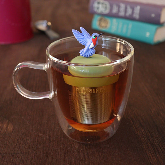 Beautiful blue hummingbird tea infuser for loose leaf tea with a fine mesh stainless steel tea strainer
that reads FLOAT2INFUSE on a green base with a tea canister and books in the background