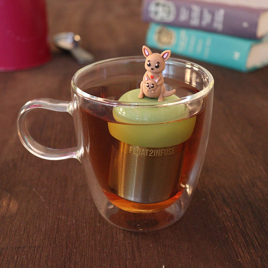 Cute mother kangaroo with a baby joey kangaroo in her pouch tea infuser for loose leaf tea with a fine mesh stainless steel tea strainer
that reads FLOAT2INFUSE on a green base with a tea canister and books in the background
