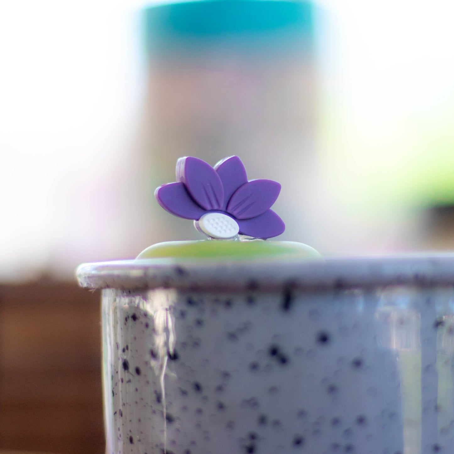 purple lotus flower tea infuser for loose leaf tea with a fine mesh stainless steel tea strainer that reads FLOAT2INFUSE on a green base floating in a blue speckled mug sitting on a coffee table 
