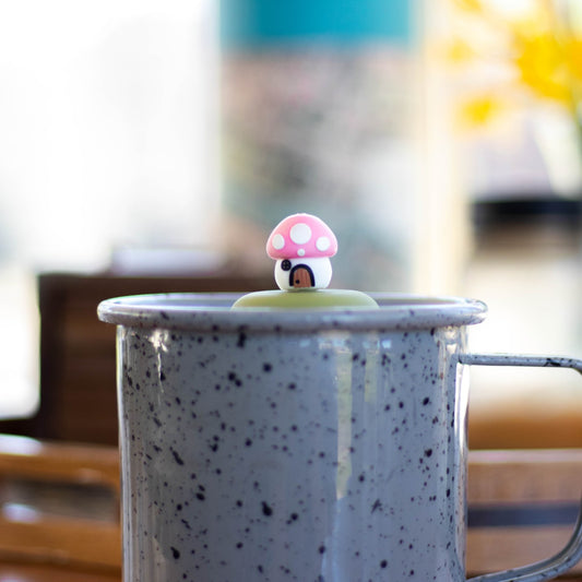 pink mushroom house tea infuser for loose leaf tea with a fine mesh stainless steel tea strainer that reads FLOAT2INFUSE on a green base floating in a speckled blue tea mug 