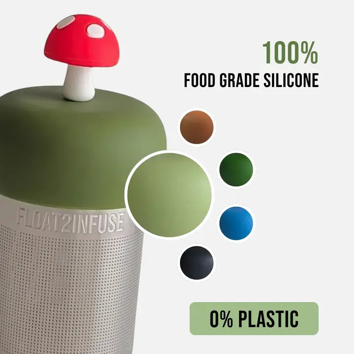 A floating tea infuser with a green floater and a red-and-white mushroom cap, shown on a light gray background with text reading '100% FOOD GRADE SILICONE' and '0% PLASTIC.' A circular inset highlights the olive green color, and small color swatches appear to the right.