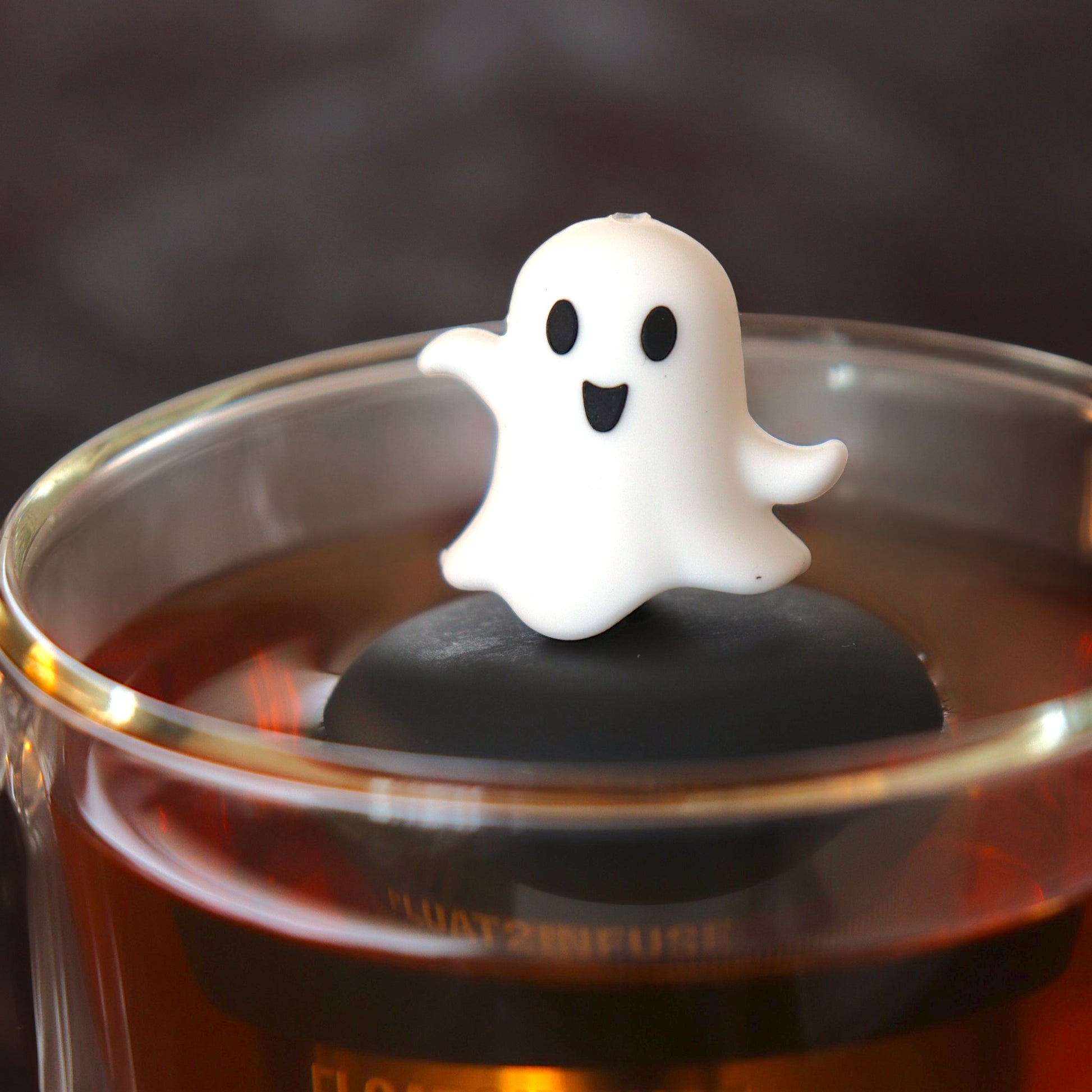 dancing white ghost tea infuser for loose leaf tea with a fine mesh stainless steel tea infuser that reads FLOAT2INFUSE on a black base floating in a glass tea mug