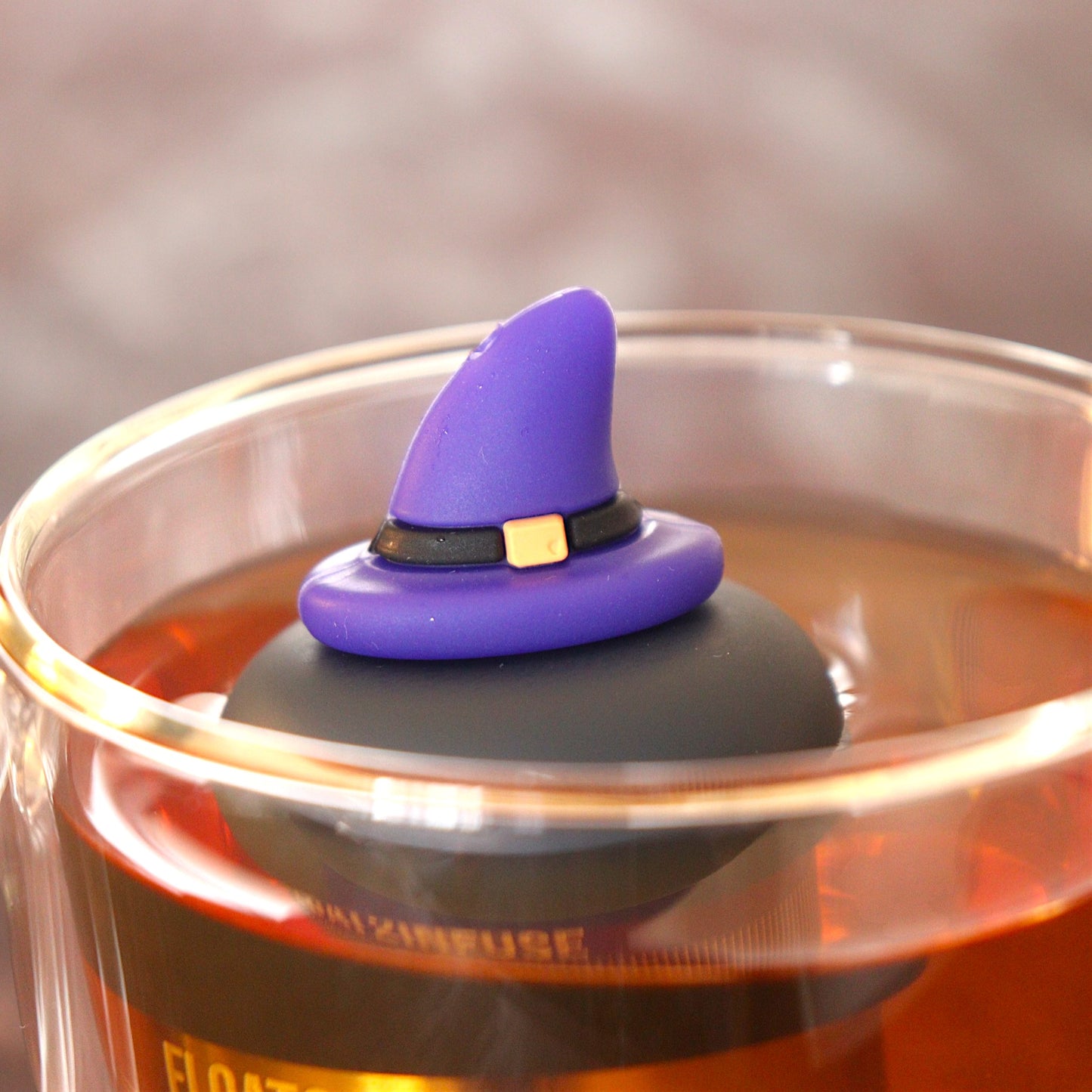 purple wizard hat tea infuser for loose leaf tea  with a fine mesh stainless steel tea infuser that reads FLOAT2INFUSEon a black base  floating in a glass tea mug