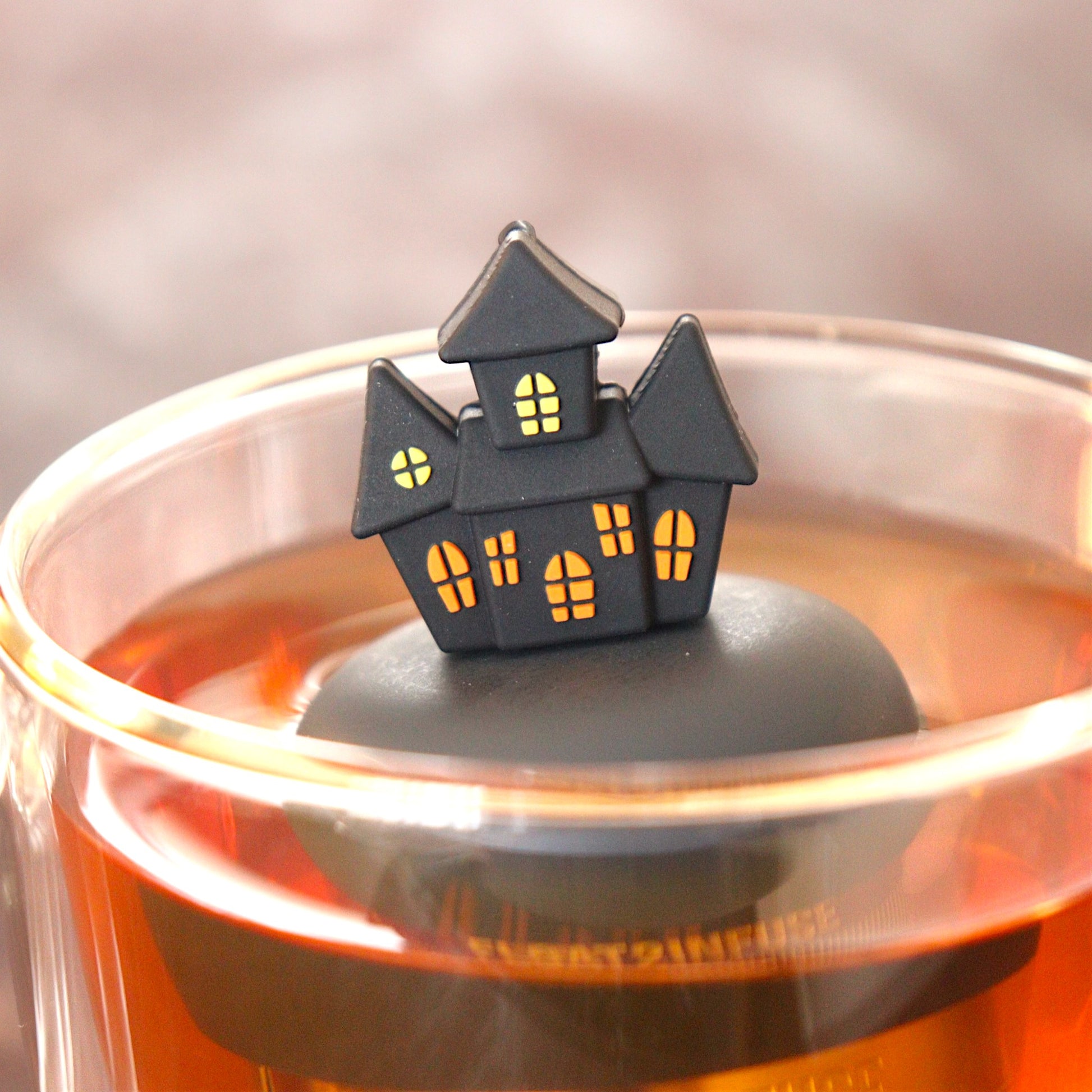 black spooky halloween house tea infuser for loose leaf tea  with a fine mesh stainless steel tea infuser that reads FLOAT2INFUSE on a black base floating in a glass tea mug