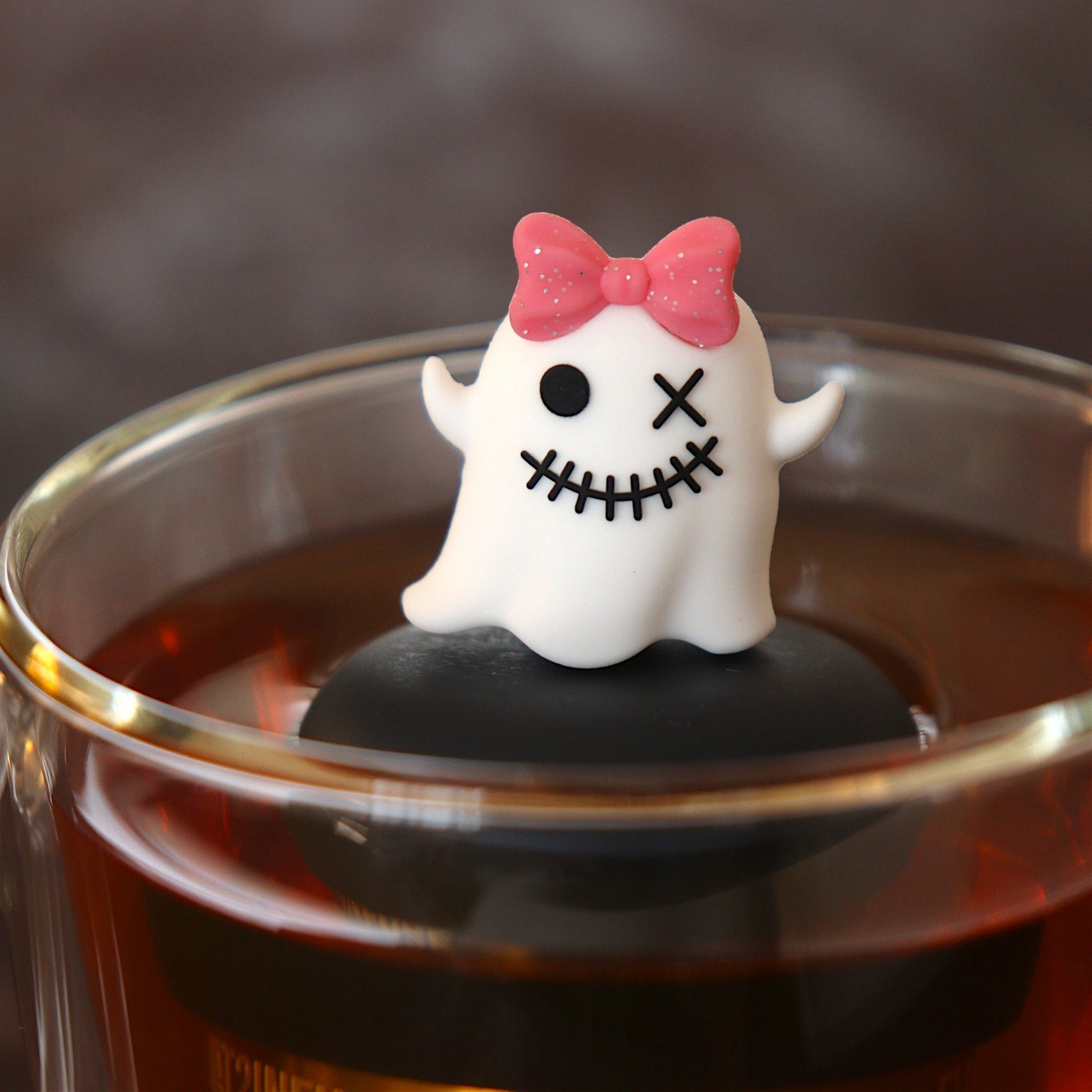 white zombie ghost with a glittery pink bow tea infuser for loose leaf tea  with a fine mesh stainless steel tea infuser that reads FLOAT2INFUSE on a black base floating in a glass tea mug