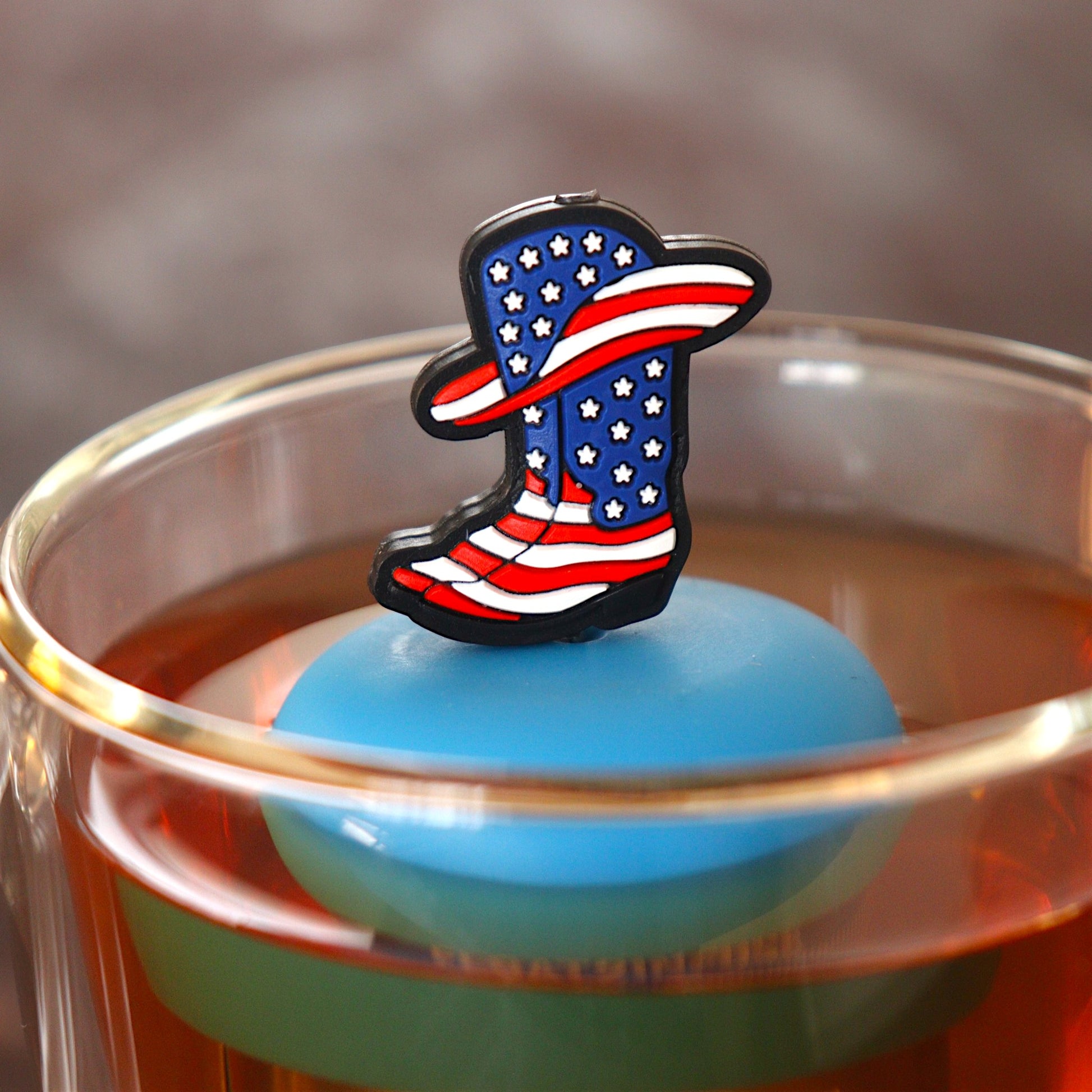 american flag patterned cowboy boots and hat tea infuser for loose leaf tea  with a fine mesh stainless steel tea infuser that reads FLOAT2INFUSE on a blue base floating in a glass tea mug