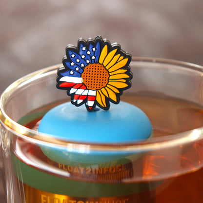 american flag patterned sunflower tea infuser for loose leaf tea with a fine mesh stainless steel tea infuser that reads FLOAT2INFUSE  on a blue base floating in a glass tea mug