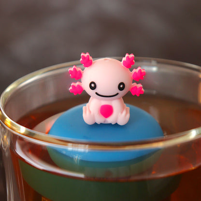 happy pink axolotl tea infuser for loose leaf tea with a fine mesh stainless steel tea strainer that reads FLOAT2INFUSE on a blue base floating in a glass tea mug