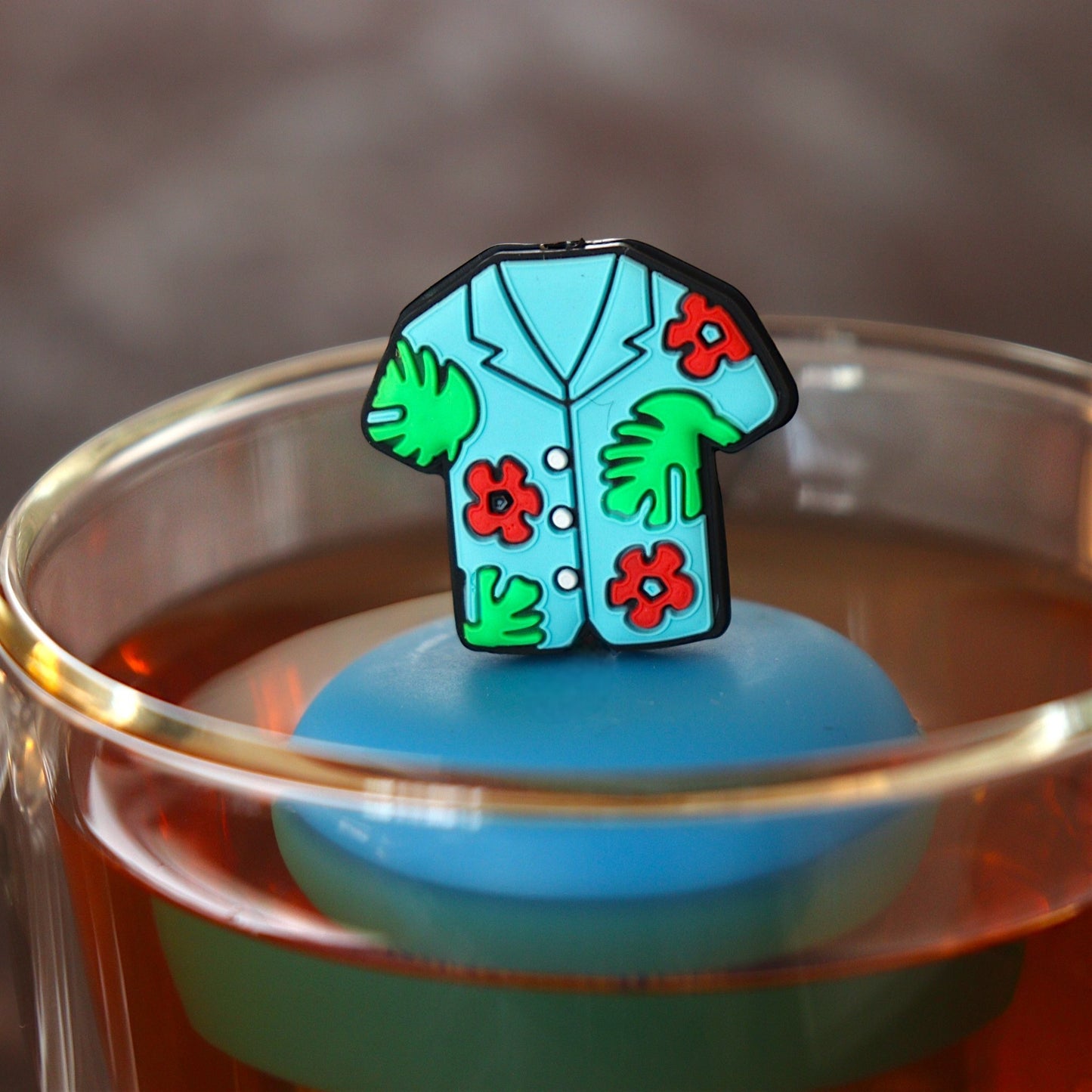 blue hawaiian shirt tea infuser for loose leaf tea with a fine mesh stainless steel tea infuser that reads FLOAT2INFUSE on a blue base  floating in a glass tea mug 