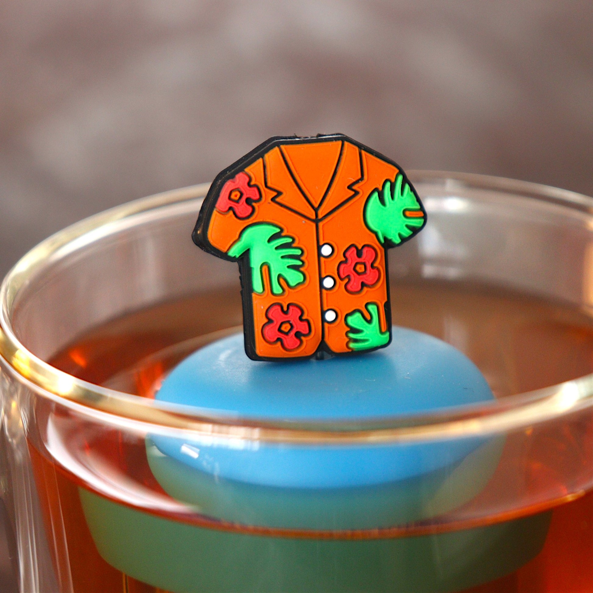 orange hawaiian shirt tea infuser for loose leaf tea  with a fine mesh stainless steel tea infuser that reads FLOAT2INFUSE on a blue base floating in a glass tea mug