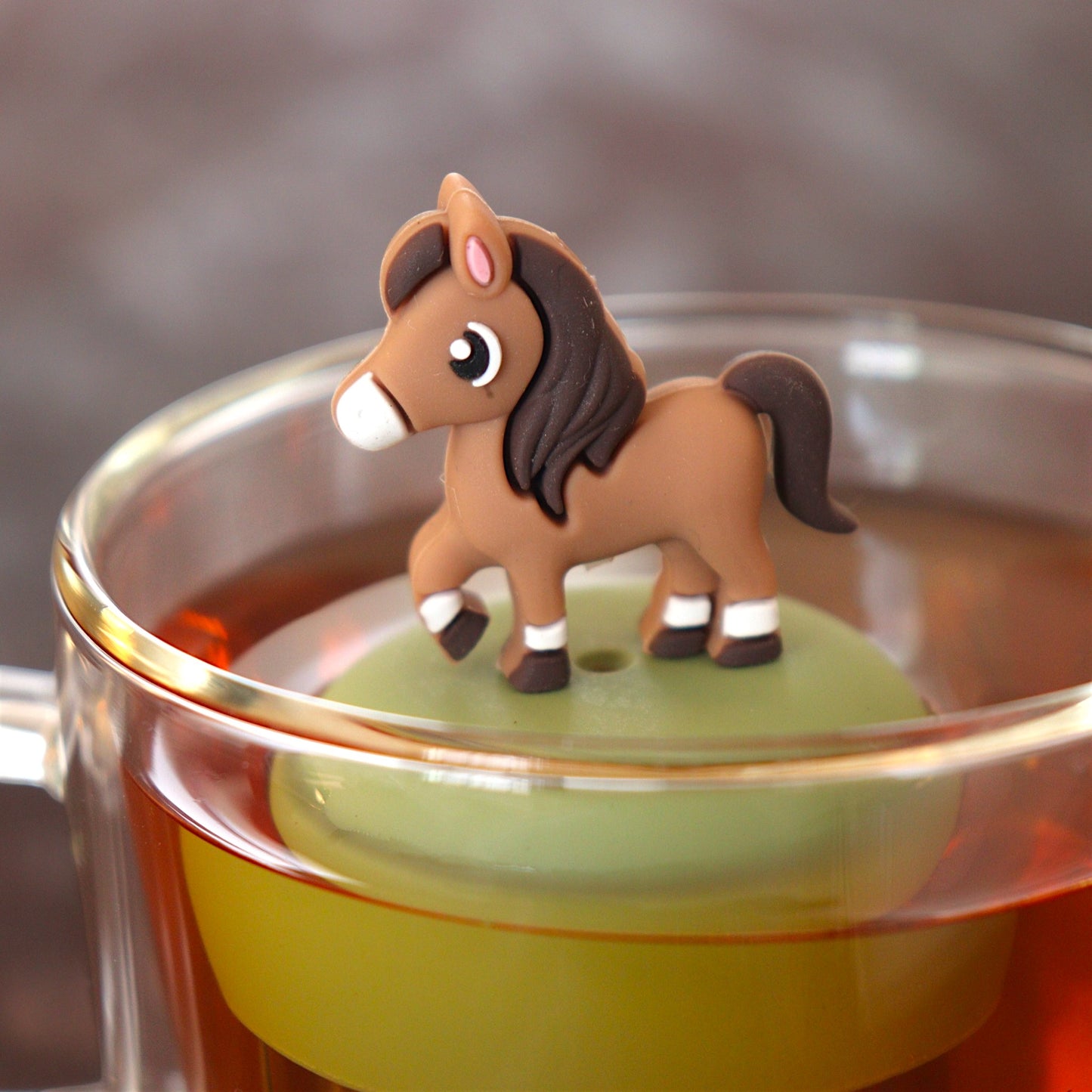 brown horse animal tea infuser for loose leaf tea  with a fine mesh stainless steel tea infuser that reads FLOAT2INFUSE on a green base floating in a glass tea mug