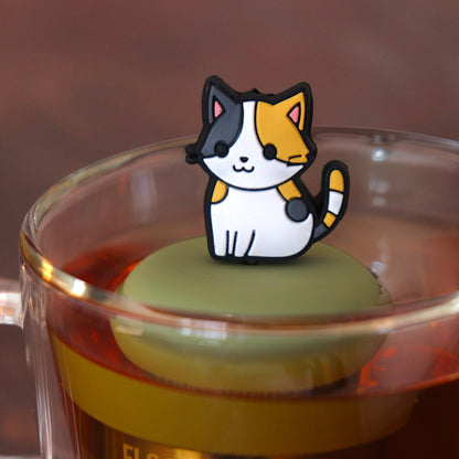 anime Calico cat tea infuser for loose leaf tea  with a fine mesh stainless steel tea infuser that reads FLOAT2INFUSE on a green base floating in a glass tea mug