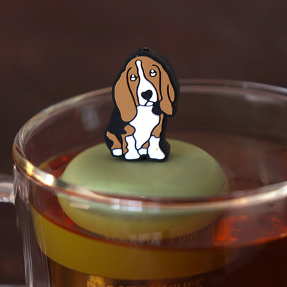 brown and white basset hound dog animal tea infuser for loose leaf tea with a fine mesh stainless steel tea infuser that reads FLOAT2INFUSE on a green base floating in a glass tea mug