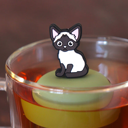 siamese cat animal tea infuser for loose leaf tea with a fine mesh stainless steel tea infuser that reads FLOAT2INFUSE on a green base  floating in a glass tea mug