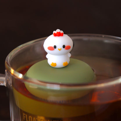 white baby chicken tea infuser for loose leaf tea with a fine mesh stainless steel tea infuser that reads FLOAT2INFUSE on a green base  floating in a glass tea mug