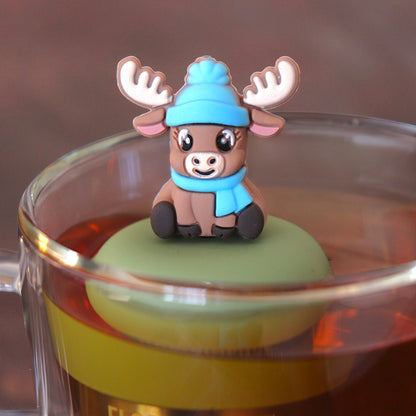 brown reindeer animal wearing blue hat and scarf tea infuser for loose leaf tea o with a fine mesh stainless steel tea infuser that reads FLOAT2INFUSE n a green base floating in a glass tea mug