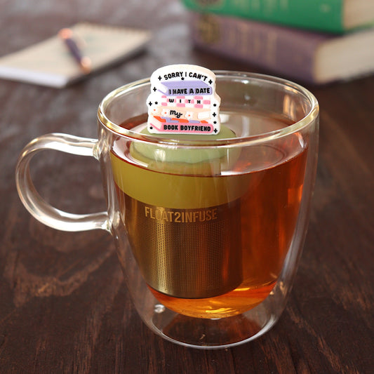 text on white background that reads "sorry i can't i have a date with my book boyfriend" on books tea infuser for loose leaf tea with a fine mesh stainless steel tea infuser that reads FLOAT2INFUSE on a green base  floating in a glass tea mug with pen on notebook and loose leaf tea and books in the background