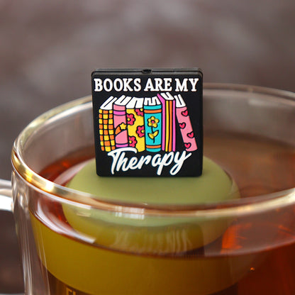 black square with text that reads "books are my therapy" on books tea infuser for loose leaf tea  with a fine mesh stainless steel tea infuser that reads FLOAT2INFUSE on a green base floating in a glass tea mug 