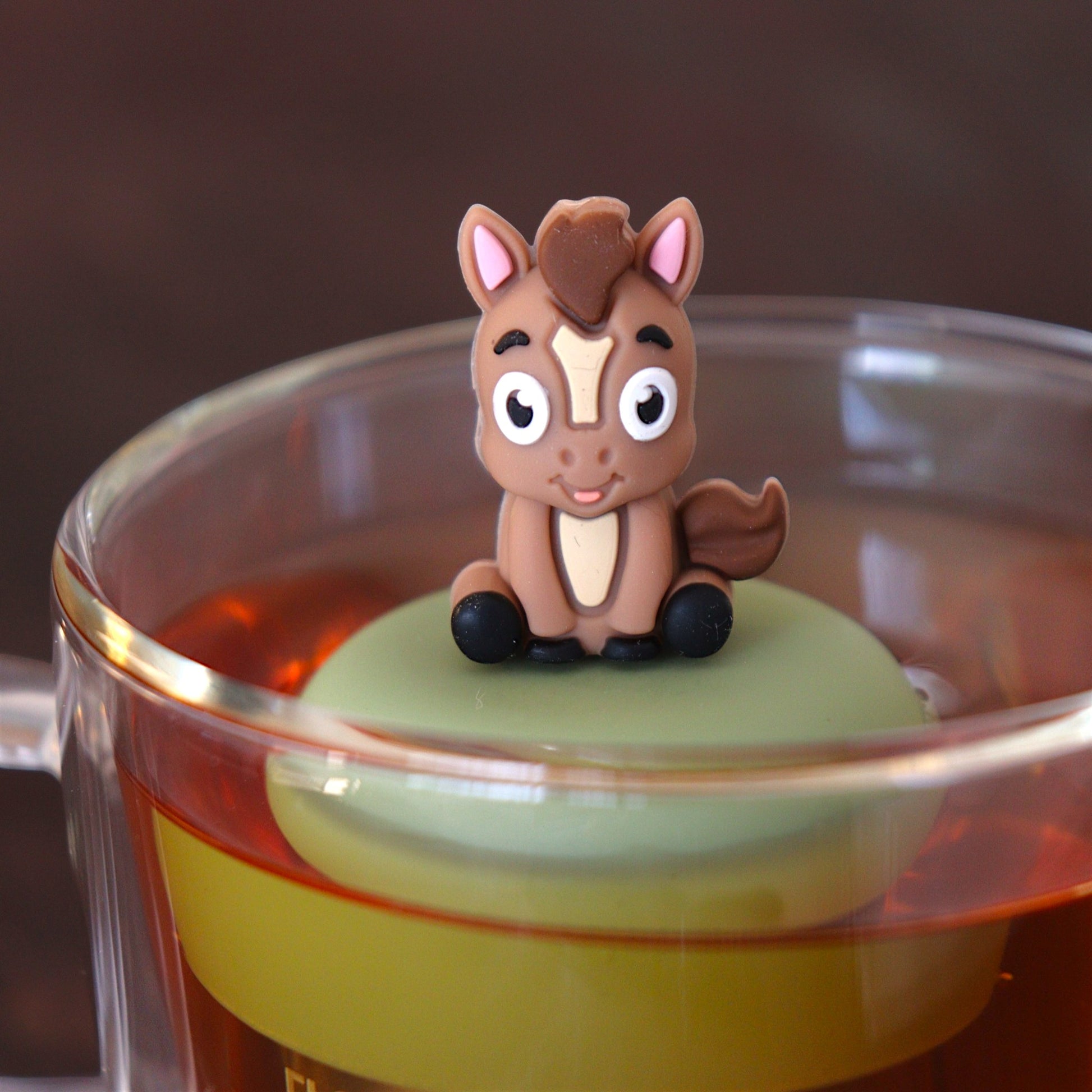 brown donkey animal tea infuser for loose leaf tea  with a fine mesh stainless steel tea infuser that reads FLOAT2INFUSE on a green base floating in a glass tea mug