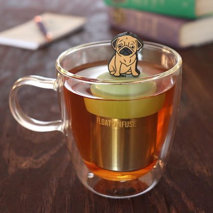 brown pug dog animal tea infuser for loose leaf tea on a green base with a fine mesh stainless steel tea infuser that reads FLOAT2INFUSE floating in a glass tea mug with pen on notebook and books in the background