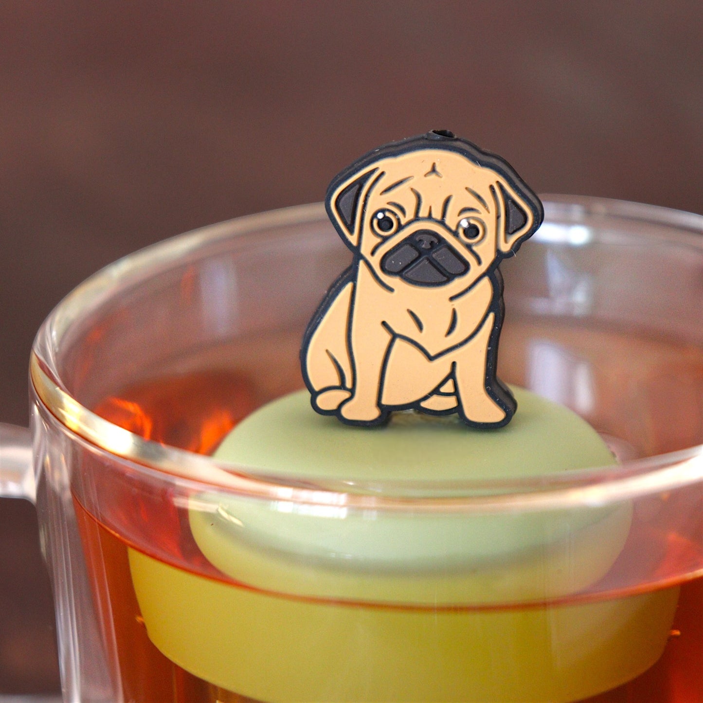 brown pug dog animal tea infuser for loose leaf tea on a green base with a fine mesh stainless steel tea infuser that reads FLOAT2INFUSE floating in a glass tea mug