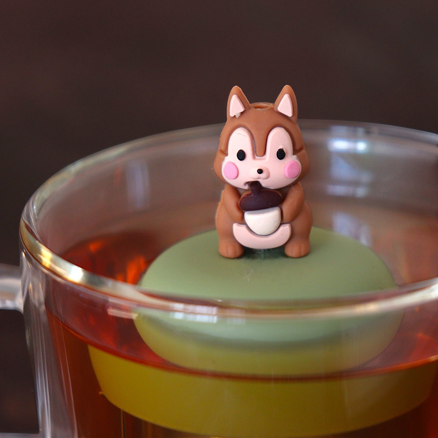 brown chipmunk tea infuser for loose leaf tea  with a fine mesh stainless steel tea infuser that reads FLOAT2INFUSE on a green base floating in a glass tea mug