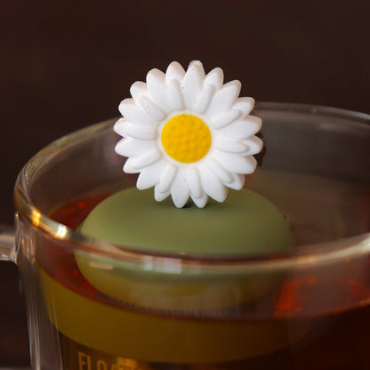 giant white daisy tea infuser for loose leaf tea  with a fine mesh stainless steel tea infuser that reads FLOAT2INFUSE on a green base floating in a glass tea mug 