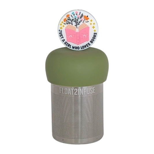 white circle that reads "just a girl who loves books" with stars and flowers coming out of a pink book tea infuser for loose leaf teawith a fine mesh stainless steel tea infuser that reads FLOAT2INFUSE  on a green base with a white background