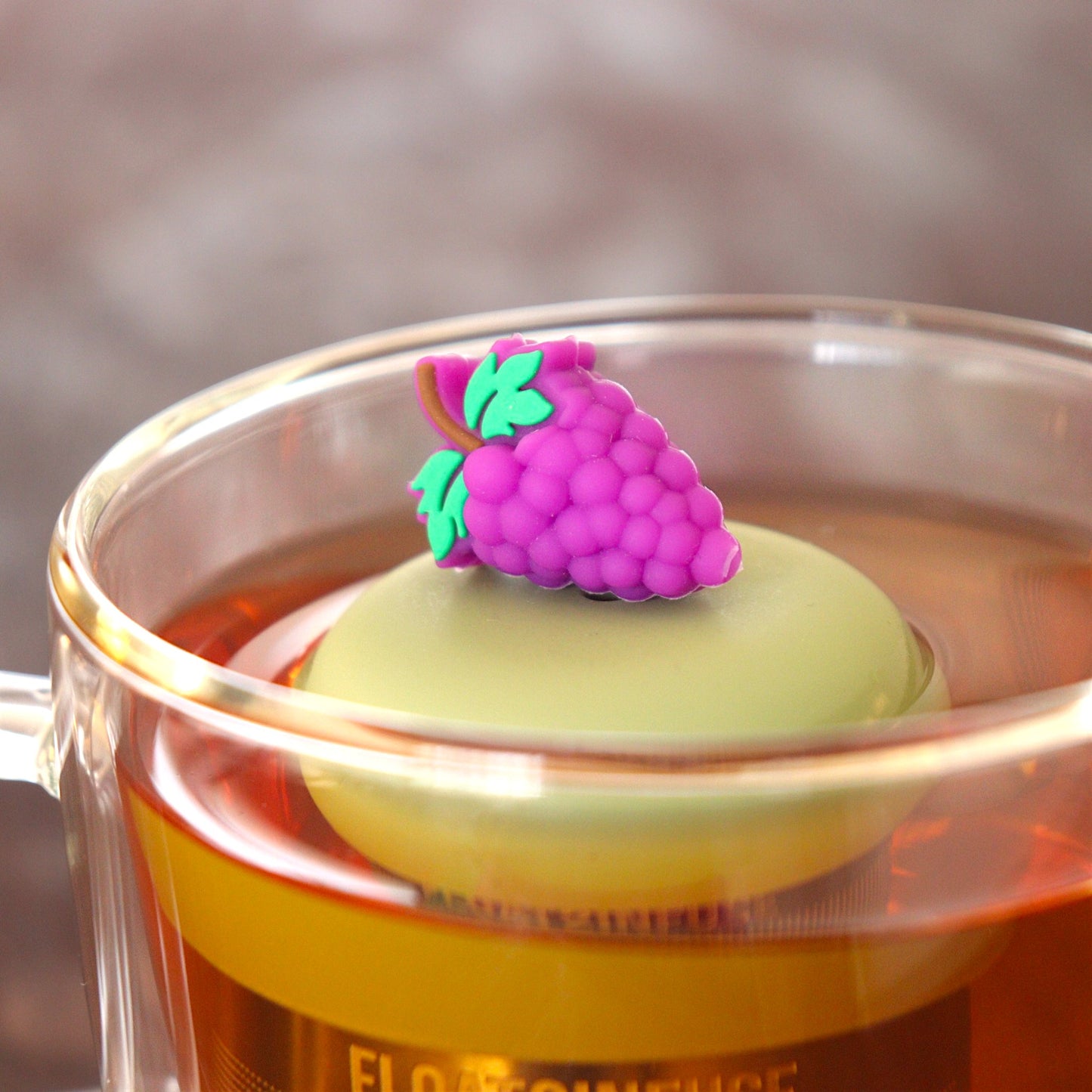 purple grapes tea infuser for loose leaf tea  with a fine mesh stainless steel tea infuser that reads FLOAT2INFUSE on a green base floating in a glass tea mug