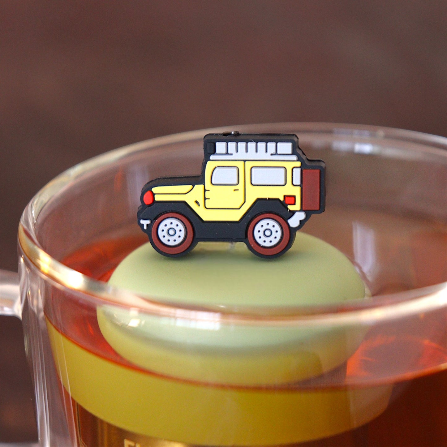 yellow jeep car tea infuser for loose leaf tea  with a fine mesh stainless steel tea infuser that reads FLOAT2INFUSE on a green base floating in a glass tea mug