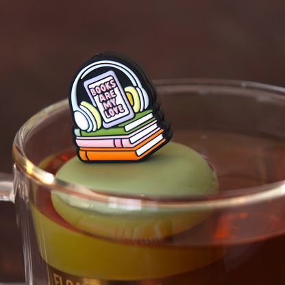 headphones on top of books that reads "books are my love" tea infuser for loose leaf tea with a fine mesh stainless steel tea infuser that reads FLOAT2INFUSE on a green base floating in a glass tea mug