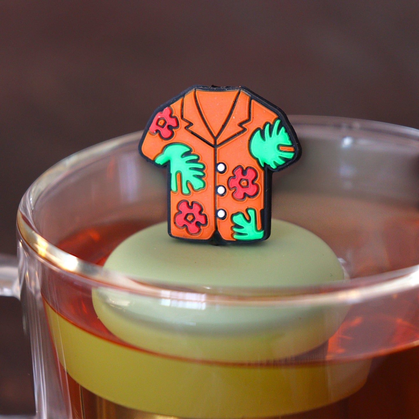 orange hawaiian shirt tea infuser for loose leaf tea  with a fine mesh stainless steel tea infuser that reads FLOAT2INFUSE on a green base floating in a glass tea mug