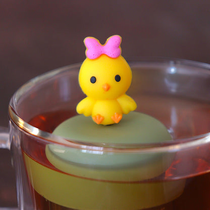 yellow chick with pink bow tea infuser for loose leaf tea  with a fine mesh stainless steel tea infuser that reads FLOAT2INFUSE on a green base floating in a glass tea mug