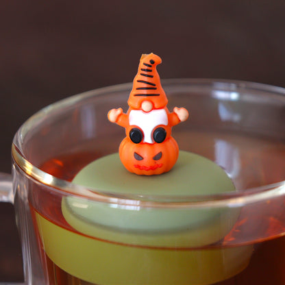 gnome sitting on pumpkin tea infuser for loose leaf tea  with a fine mesh stainless steel tea infuser that reads FLOAT2INFUSE on a green base floating in a glass tea mug
