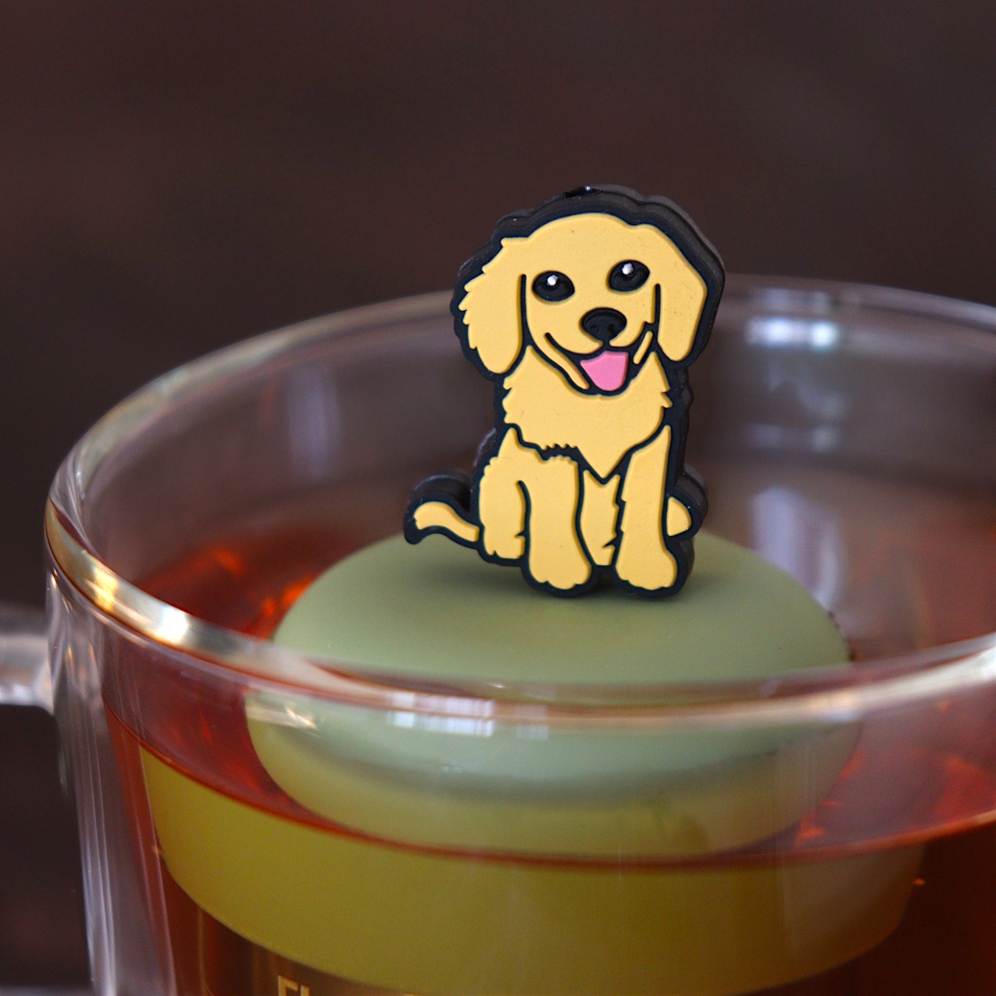yellow smiling dog animal tea infuser for loose leaf tea on a green base with a fine mesh stainless steel tea infuser that reads FLOAT2INFUSE floating in a glass tea mug 