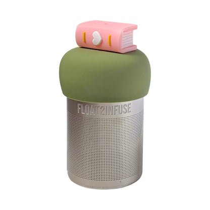 Light pink book with a white heart on the spine tea infuser for loose leaf tea with a fine mesh stainless steel tea strainer that reads FLOAT2INFUSE on a green base with a white background