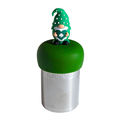 Cute gnome dressed all in green holding a green heart with a white shamrock tea infuser for loose leaf tea with a fine mesh stainless steel tea strainer that reads FLOAT2INFUSE on a dark green base with a  white background
