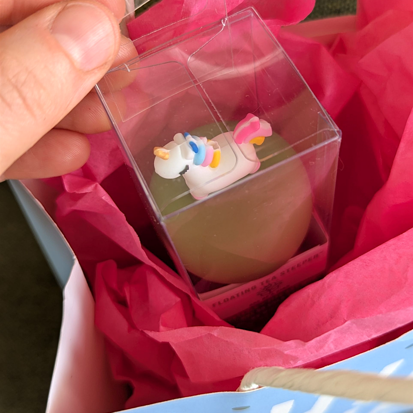 someone is unwrapping a floating unicorn tea infuser in a gift bag