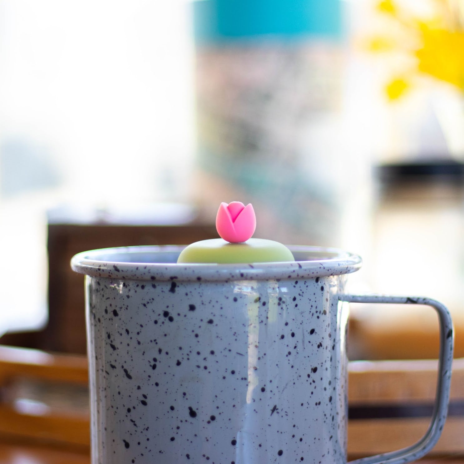 pink tulip flower tea infuser for loose leaf tea with a fine mesh stainless steel tea strainer that reads FLOAT2INFUSE on a green base floating in a speckled blue tea mug 