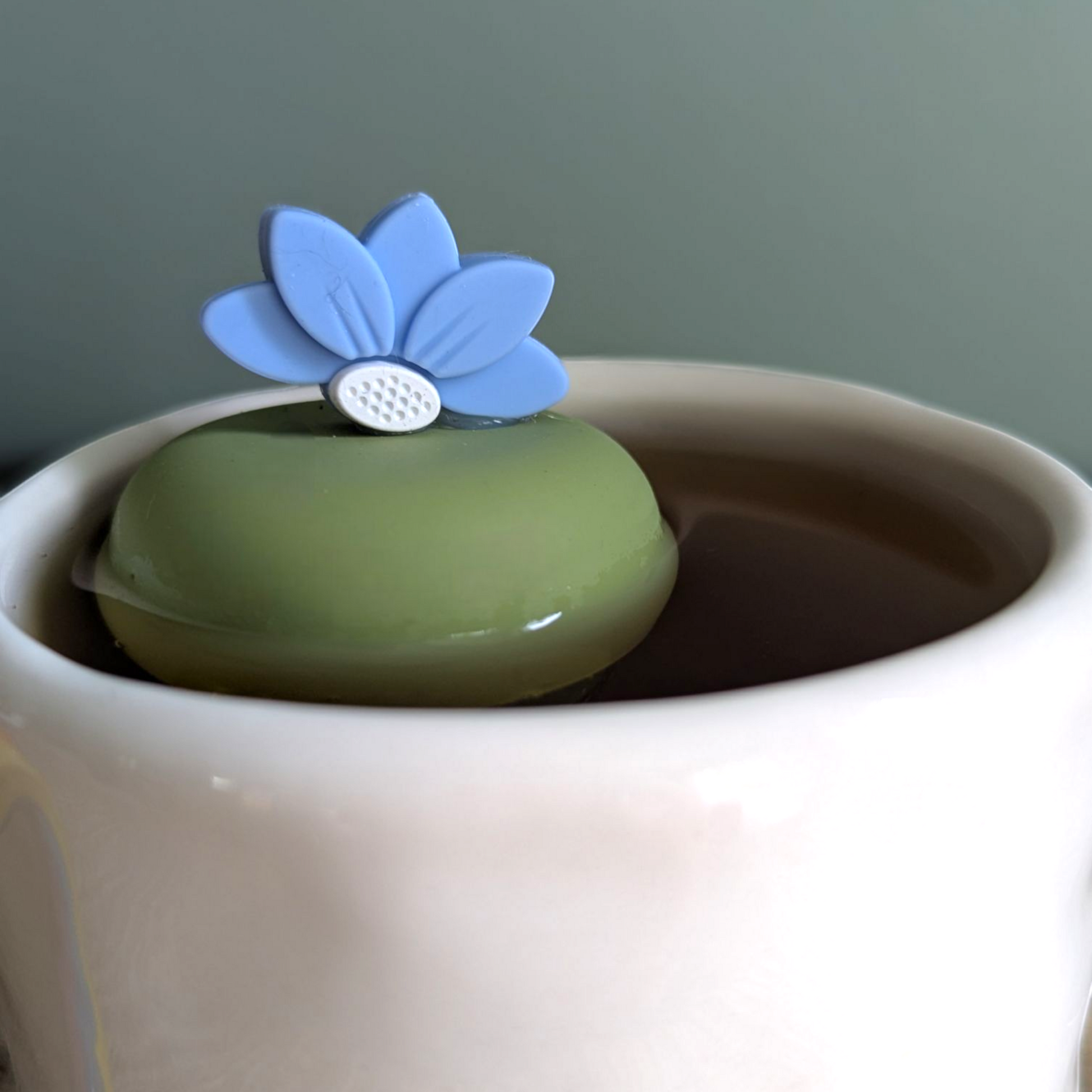 blue lotus flower tea infuser for loose leaf tea  with a fine mesh stainless steel tea infuser that reads FLOAT2INFUSE on a green base floating in a white tea mug 