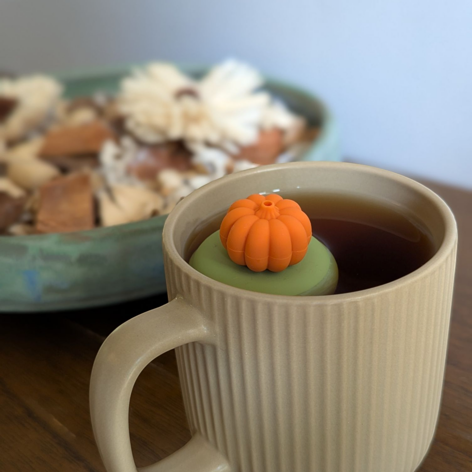 3D orange pumpkin tea infuser for loose leaf tea with a fine mesh stainless steel tea strainer that reads FLOAT2INFUSE on a green base  floating in a beige tea mug with potpourri in the background